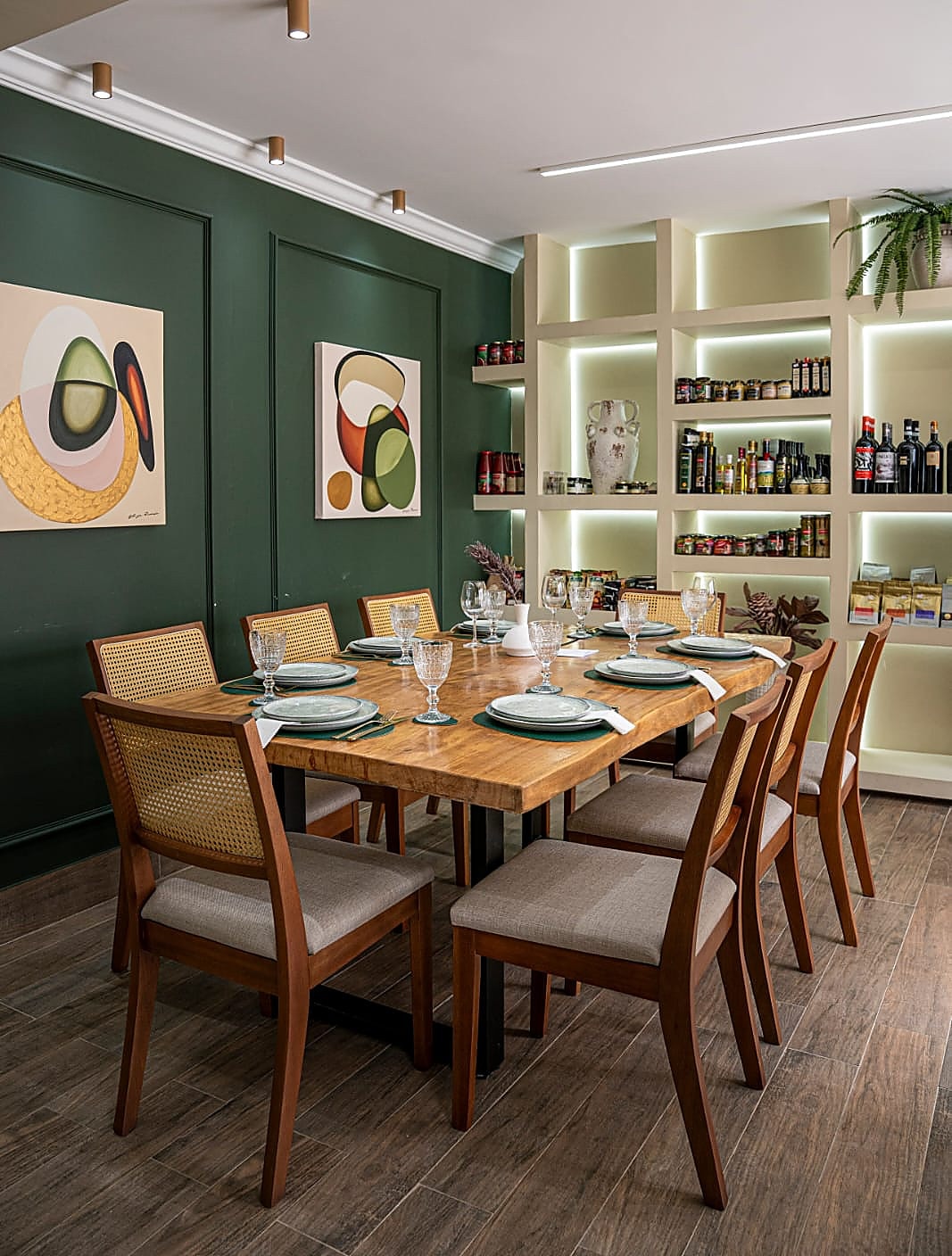 Sala de jantar com parede verde, quadros coloridos e mesa de madeira posta