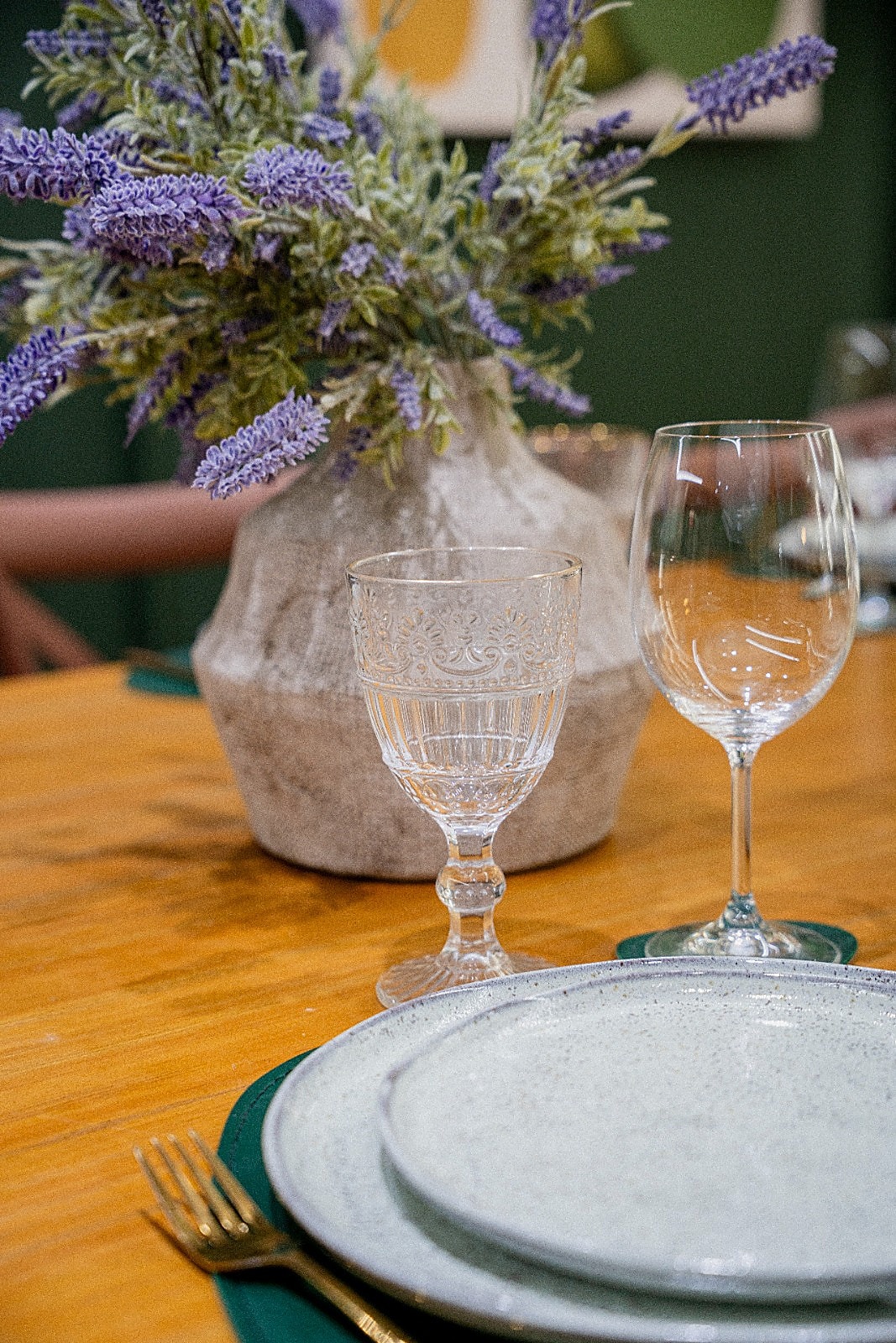 Taças de cristal e vaso de flores lilás sobre mesa de madeira em ambiente verde